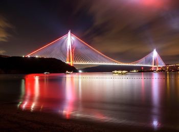 Illuminated cable-stayed bridge over river against sky at night