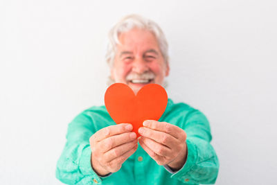 Portrait of a serious young woman holding heart shape over white background