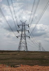 Low angle view of electricity pylon on field against sky