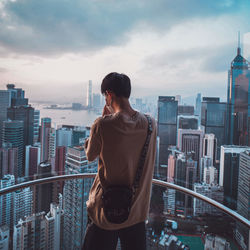 Rear view of man looking at city buildings against sky