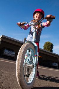 Low angle view of girl riding bicycle on road against blue sky