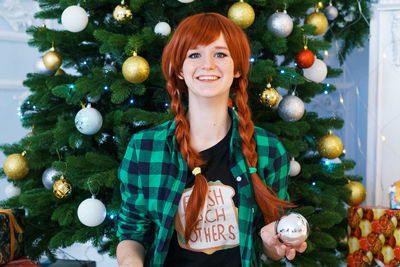 Charming smiling red-haired young woman in plaid shirt, against the background