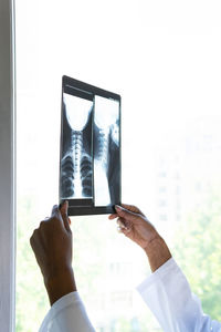 Crop black female medic standing near window and examining x ray scan while working in clinic