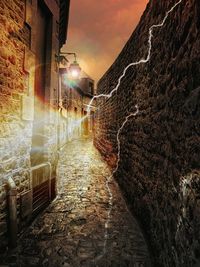 Walkway amidst illuminated buildings against sky