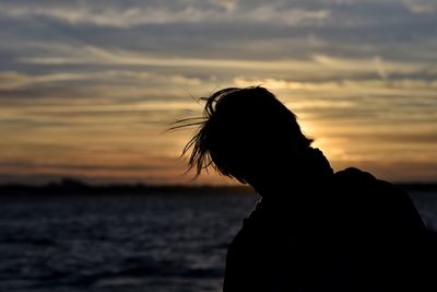 Silhouette woman standing at beach against sky during sunset