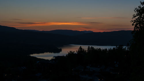 Scenic view of lake and silhouette mountains against sky at sunset