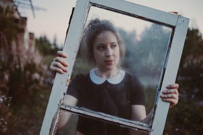 Portrait of young woman holding camera while standing outdoors