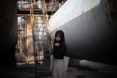 Portrait of young woman standing by pipe at industry