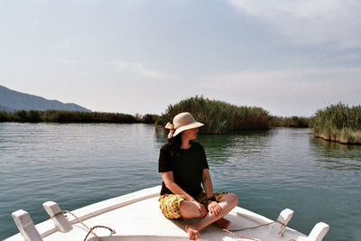 Woman sitting by lake against sky