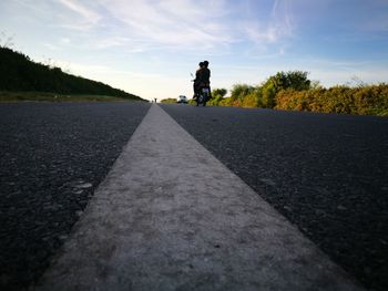 Rear view of woman walking on road by trees against sky