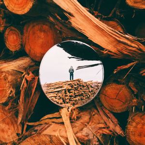Reflection of man on stack of logs