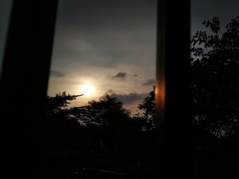 Silhouette trees against sky during sunset seen through window