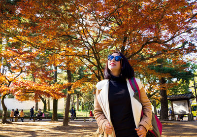 Young woman standing by trees during autumn