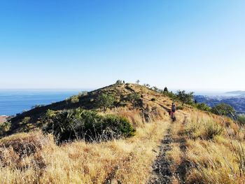 Scenic view of hill high above the sea against clear sky, mother and daughter walking. 