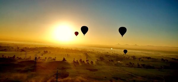 Hot air balloons flying over landscape against sky during sunset