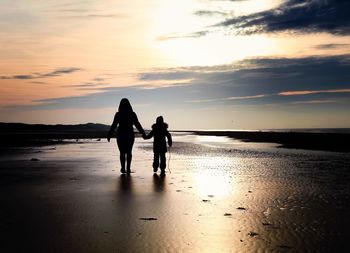 Silhouette friends on beach against sky during sunset