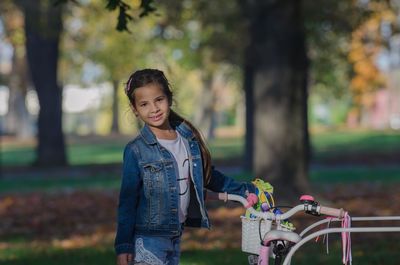 Portrait of smiling cute girl standing by bicycle at park