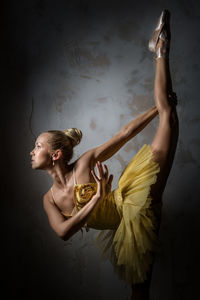 Beautiful ballerina dancing against wall in dark