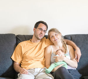 Happy mother and father holding baby at sofa at home