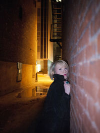 Woman leaning against brick wall in alley at night