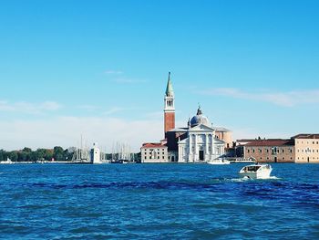 Boat sailing on sea by city against sky