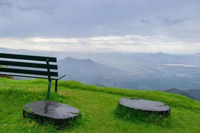 Empty bench by mountains against sky