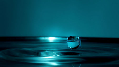 Macro shot of drop falling on water against colored background