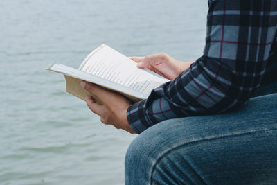 Midsection of man reading book against sea