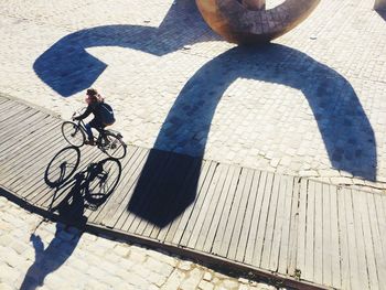High angle view of woman cycling on boardwalk during sunny day
