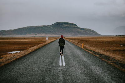 Rear view of man walking on road against sky