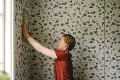 Side view of woman adjusting picture frame on wall at home
