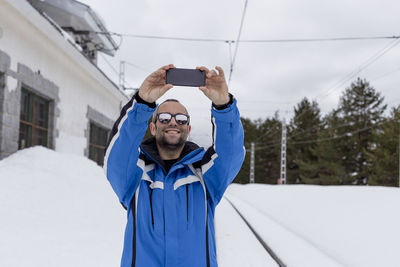 Portrait of smiling man standing on snow covered camera