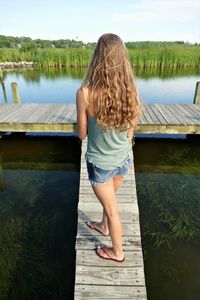 Rear view of woman standing by swimming pool against lake