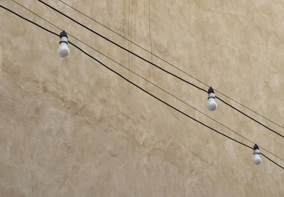Low angle view of light bulbs hanging by concrete wall