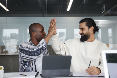 Smiling coworkers sitting at business meeting and giving each other high five