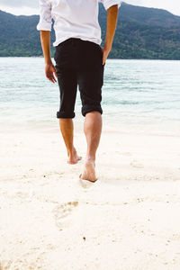 Low section of man walking on shore at beach