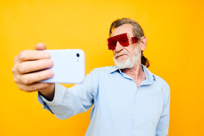 Senior man using smart phone against yellow background