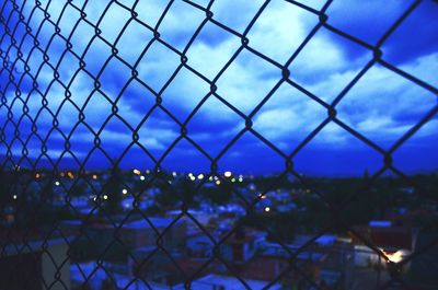 City seen through chainlink fence against cloudy sky 