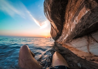 Low section of person by sea against sky during sunset