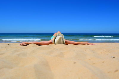 Low section of woman sitting on beach against clear sky