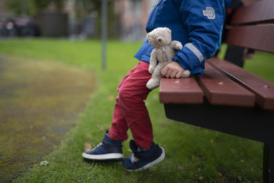 A lonely boy sitting on a bench with his teddy bear in hand