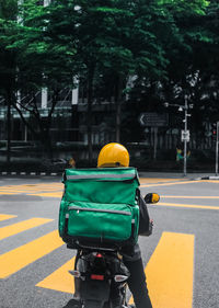 Rear view of delivery man riding motor scooter on street