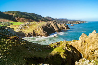 Scenic view of sea and mountains against clear blue sky