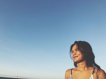 Young woman smiling against clear blue sky