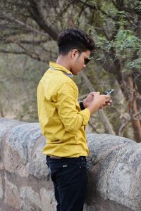 Side view of young man using phone while standing on rock