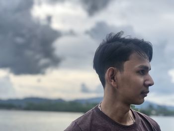 Portrait of young man looking away against sky