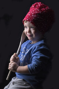 Boy holding wooden spoon while sitting against black background