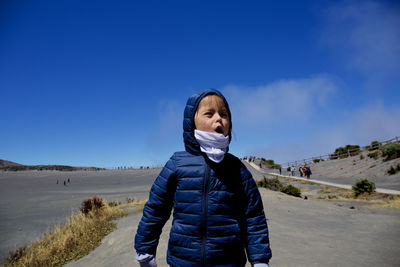 Cute girl wearing warm clothing while standing on land against sky during sunny day