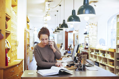 Young female sales clerk talking on mobile phone while looking at file in home improvement store