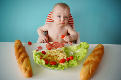 A child eats sausage with pasta and baguette